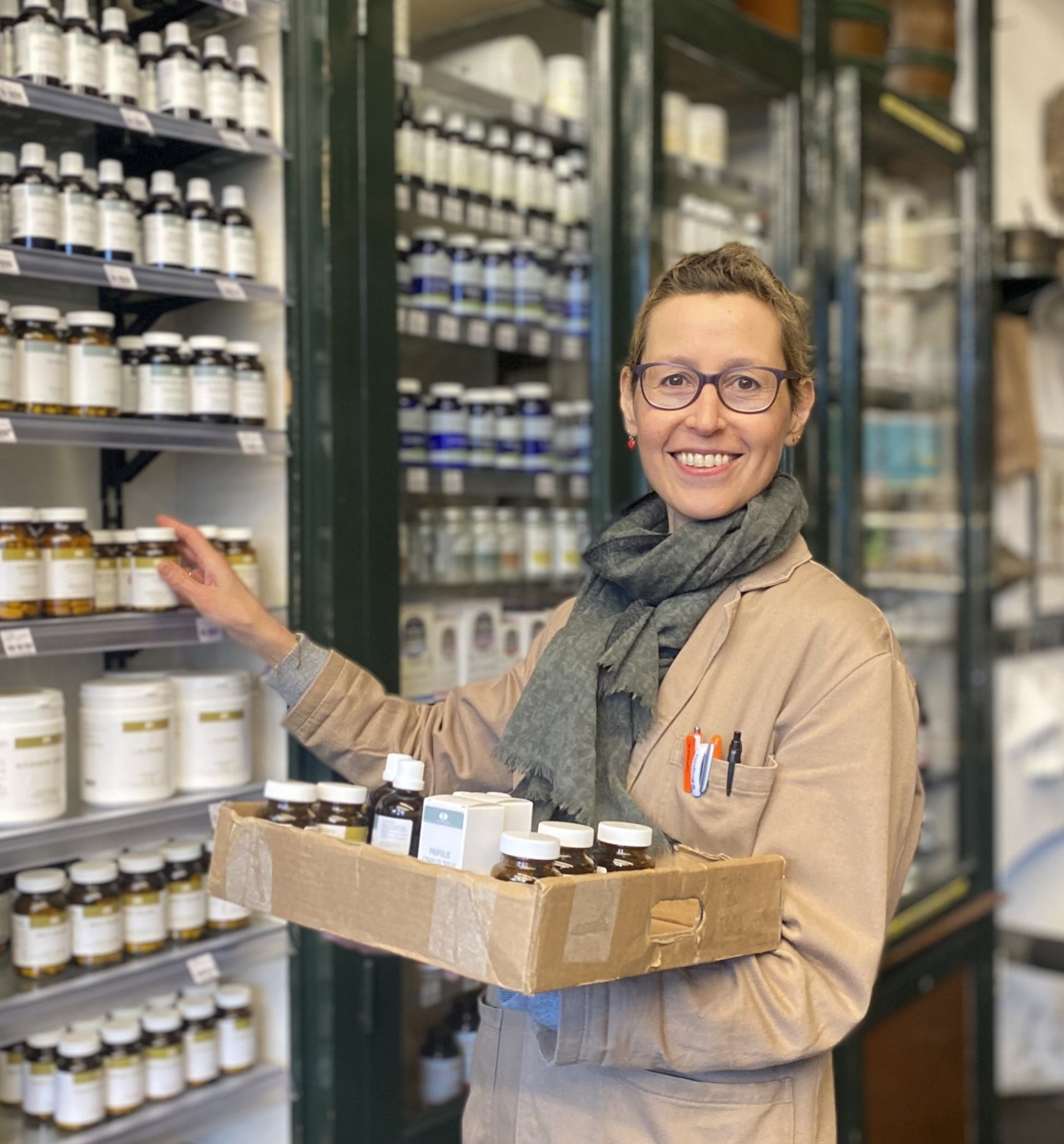 Lachende winkelmedewerker Maud, vrouw met bril en stofjas en tray met producten