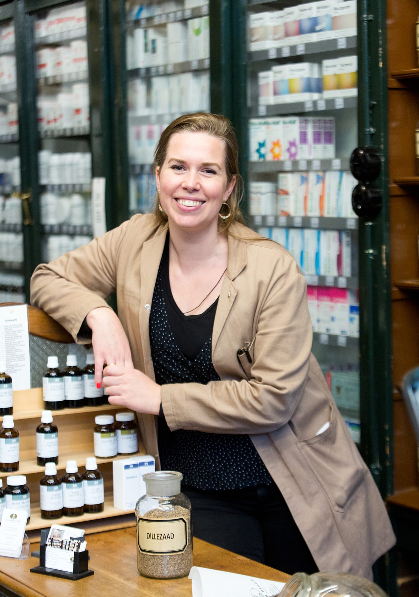 lachende medewerker roseline met stofjas en zwart shirt in de winkel bij de flesjes bij de toonbank
