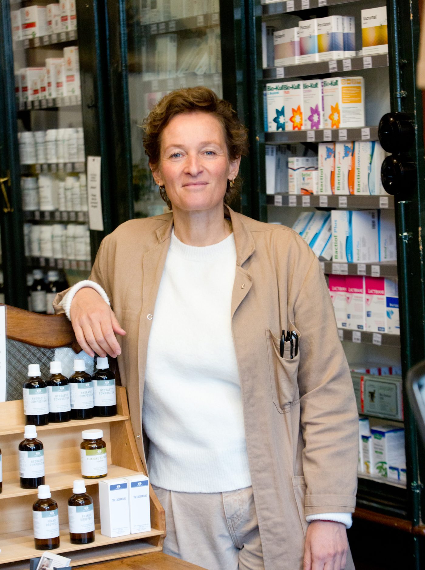 Lachende Petra Vlieger in de winkel met stofjas aan, licht leunend